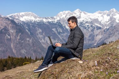 Genç adam dağlarda dizüstü bilgisayar kullanıyor.