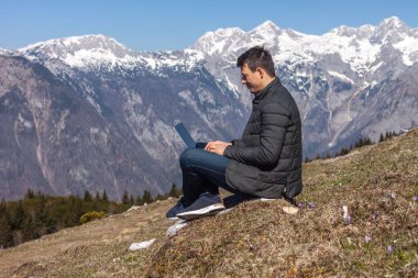 Genç adam dağlarda dizüstü bilgisayar kullanıyor.