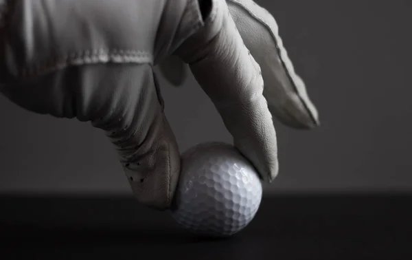 Mão em luva manter bola de golfe no fundo preto — Fotografia de Stock
