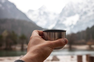 Erkek eli termos bardağını dışarıda gezdirir.