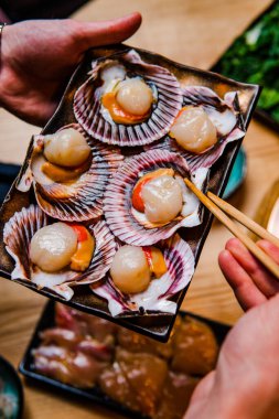 Yemek çubukları ve lezzetli deniz tarakları tutan birinin kırpılmış fotoğrafı.