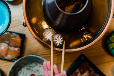Yemek çubuğu tutan ve geleneksel Asya sıcak tenceresinde yemek hazırlayan kişinin kısmi görüntüsü 