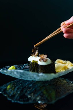 Somonlu suşi ve tabakta avokado. Çubuklu insan eli.