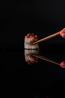 Lezzetli suşi ve siyah arka planda yemek çubukları.