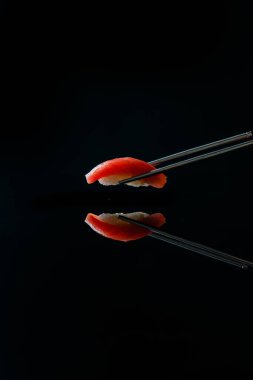 Japon suşisi, ton balığı ve yemek çubuklarıyla siyah arka planda yakın plan görüntüsü. 