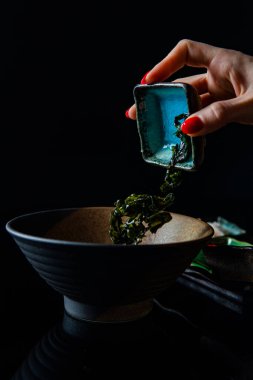 Kırpılmış bir kadın yemek pişirirken kaseye malzeme ekliyor.