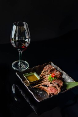 Sebzeli ve soslu ızgara et, siyah arka planda bir bardak şarap.