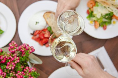 Bardakları tokuşturup, restoranda yemek yiyen insanların görüntüsü.