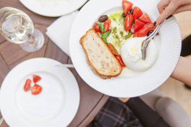 Domatesli, mozzarellalı ve fesleğenli lezzetli salata yiyen bir kadın resmi. 