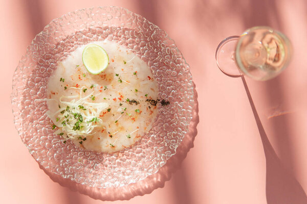 вид на изысканное блюдо, украшенное лаймом и бокалом вина на розовой поверхности
