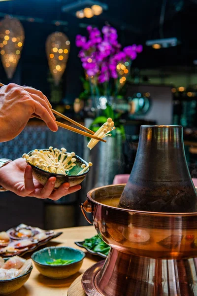 キノコとおいしいアジアの鍋料理を準備する人の切り取られたショット ロイヤリティフリーのストック画像
