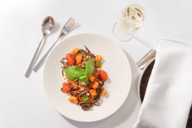 Beyaz tabakta deniz ürünleri ve sebzeli spagetti ve beyaz yüzeyde şarap.