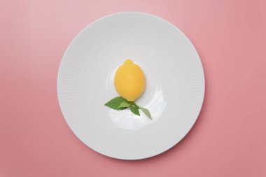 Yeşil yapraklı sarı limon üst görünümü beyaz yuvarlak plaka üzerinde pembe arka plan