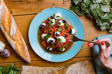 Lezzetli domates, mozarella ve fesleğen salatası yiyen bir kadının kısmi görüntüsü. 