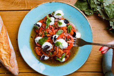 Lezzetli domates, mozarella ve fesleğen salatası yiyen bir kadının kısmi görüntüsü. 