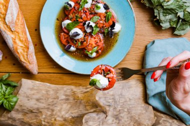 Lezzetli domates, mozarella ve fesleğen salatası yiyen bir kadının kısmi görüntüsü. 