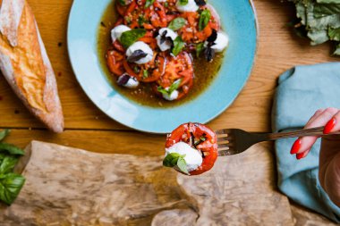 Lezzetli domates, mozarella ve fesleğen salatası yiyen bir kadının kısmi görüntüsü. 