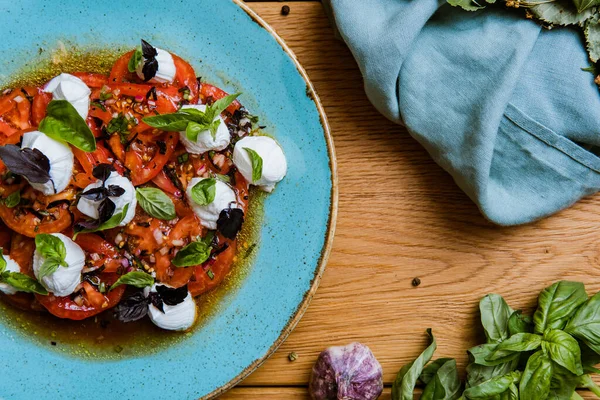 Lezzetli domates, mozarella ve ahşap masada fesleğen salatası.