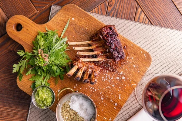 Ahşap tahtada soslu ve sebzeli ızgara pirzola ve restorandaki masada bir bardak kırmızı şarap.