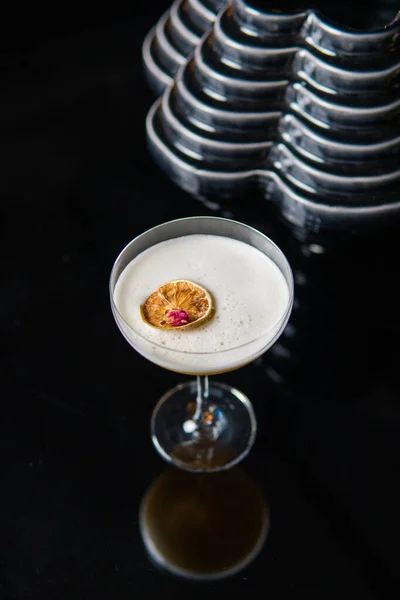 close-up view of glass of white cocktail with citrus fruit slice reflected on black background