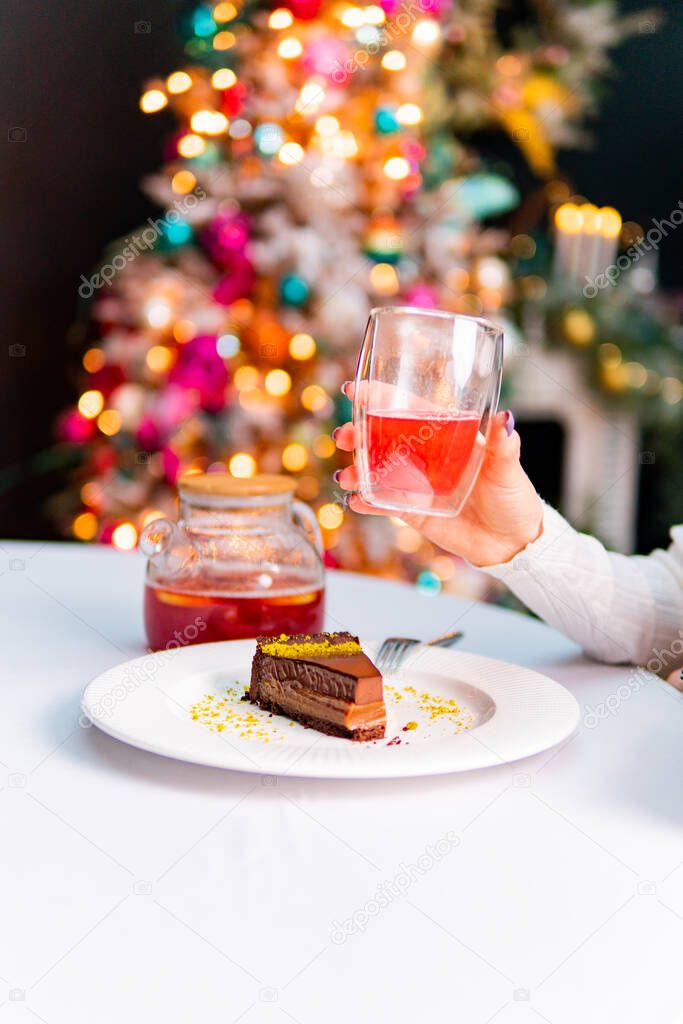 close-up of a festive table decorated with christmas decorations on the background. cropped shot of woman eating tasty dessert and drinking refreshing beverage