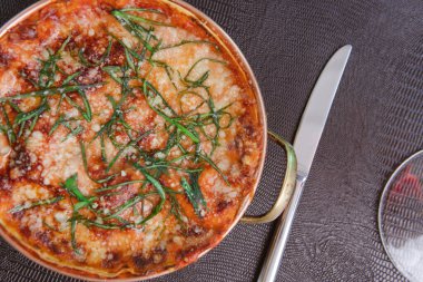 Gri yüzeyde jambonlu, peynirli ve domatesli lezzetli pizza manzarası.