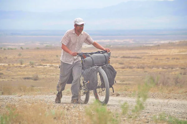 Bisikletçi, Güney Kazakistan 'da dolu bir turist bisikletinin yanında yürüyor