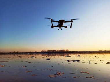 Quadcopter gün batımında nehrin üzerinde uçuyor.