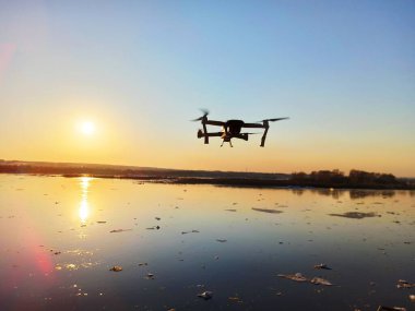Quadcopter gün batımında nehrin üzerinde uçuyor.