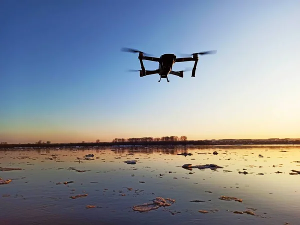 Quadcopter gün batımında nehrin üzerinde uçuyor.