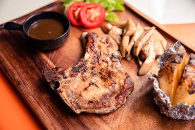 Kızarmış kurobuta domuz pirzolası sotelenmiş mantar, patates kaması ve ahşap kesim tahtasının üzerinde kara biber sosu.