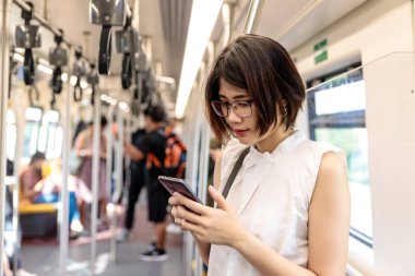 Trende akıllı telefonunu kullanan ve ona bakan kısa saçlı Asyalı bir kadın.