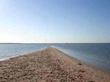Kum kayalığı denize dökülür, deniz her iki taraftadır. Kumda ayak izleri.
