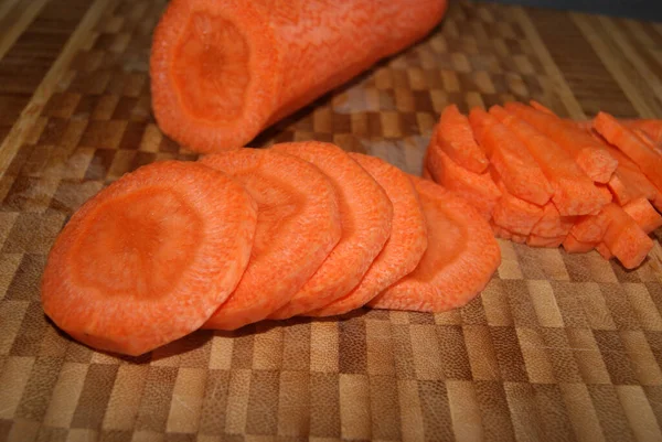 A piece of peeled carrots and carrots cut into slices and bars lies on the cutting board