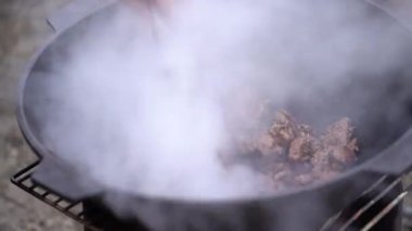Adam eti tencereye koyup ateşe atıyor.