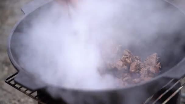 De man zet het vlees in een pot boven een open vuur — Stockvideo