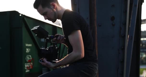 Mannelijke jonge filmmaker in het zwart met baard film handheld de zonsondergang. Ondernemingen — Stockvideo