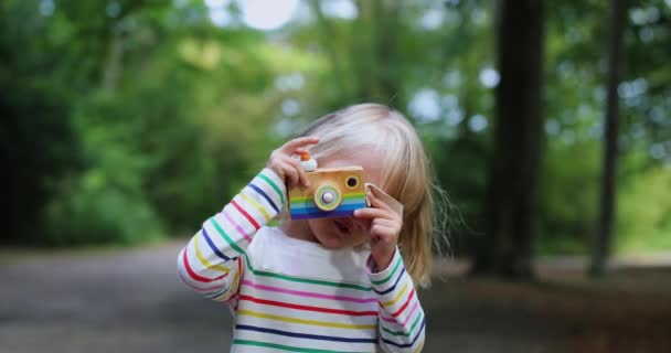 Mała dziewczynka robi zdjęcia z aparatem blondynka drewniany aparat — Wideo stockowe