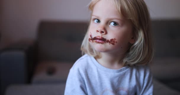 Κοντινό πλάνο αστείο βρώμικο μικρό κορίτσι τρώει σοκολάτα. Καστανά χείλη και δόντια. — Αρχείο Βίντεο