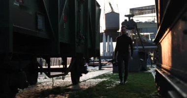 Erkek sinemacı büyük bir şehirde gün batımında kamerayla yürür. Sanayi