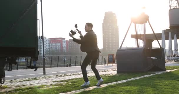 Cinéaste sauter avec la caméra à la main sur le coucher du soleil dans une grande ville. Industriel — Video