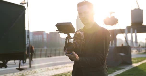 Hombre Cineasta sonrisa en la cámara al atardecer en una gran ciudad. Industrial — Vídeo de stock