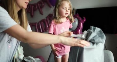 Sarışın küçük kız hediyeleri açıyor. Çocuk kutuya bakar, şaşırır.