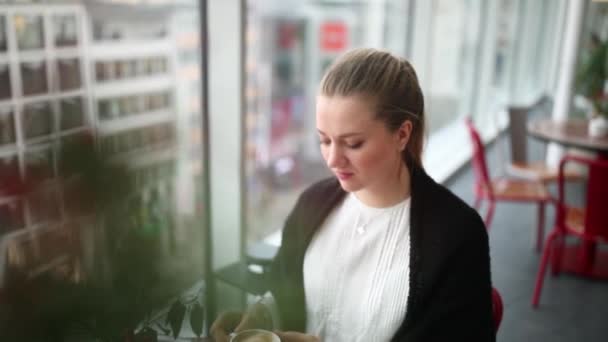 Menina com cabelo loiro longo bebe café em um café perto da janela — Vídeo de Stock