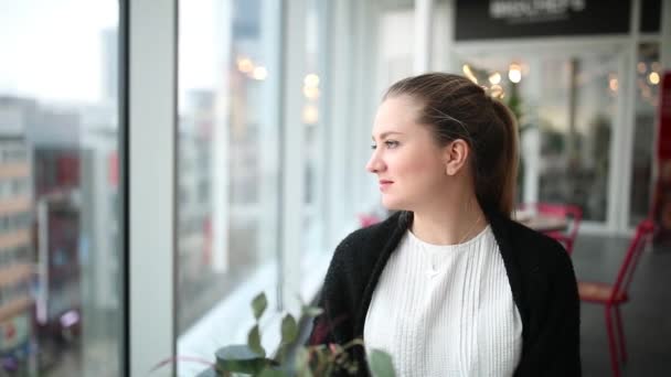 Beautiful girl looks out the window and smiles — Stock Video