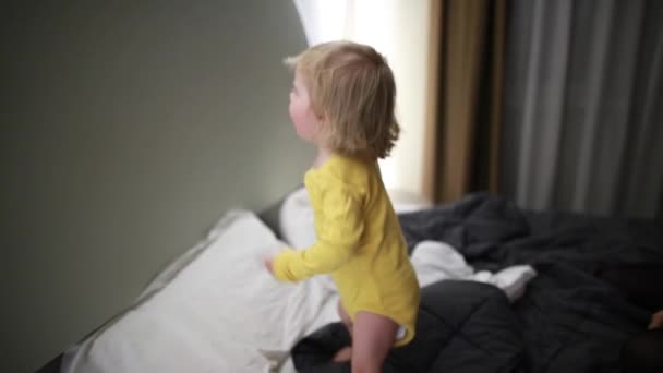 Щаслива маленька дитина стрибає на батьківському ліжку — стокове відео
