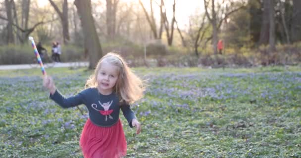 Блондинка счастливо кружится в красивом платье в весеннем парке — стоковое видео