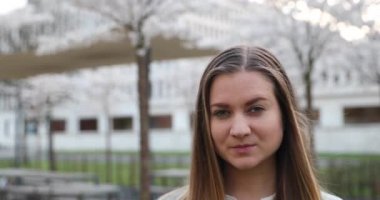 Sarışın, uzun saçlı, şehirde yapay ağaçların yanında duruyor.