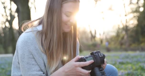 Ung blondin med långt hår fotograferar på kameran i vår park — Stockvideo
