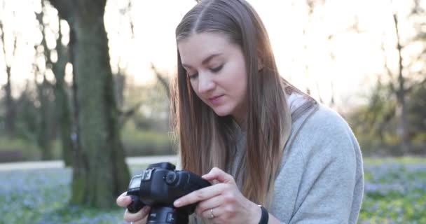 Блондинка с длинными волосами в весеннем парке снимает на камеру и смотрит кадры — стоковое видео
